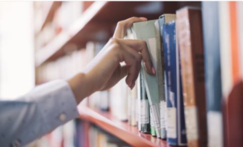 A hand reaching for a book on a shelf